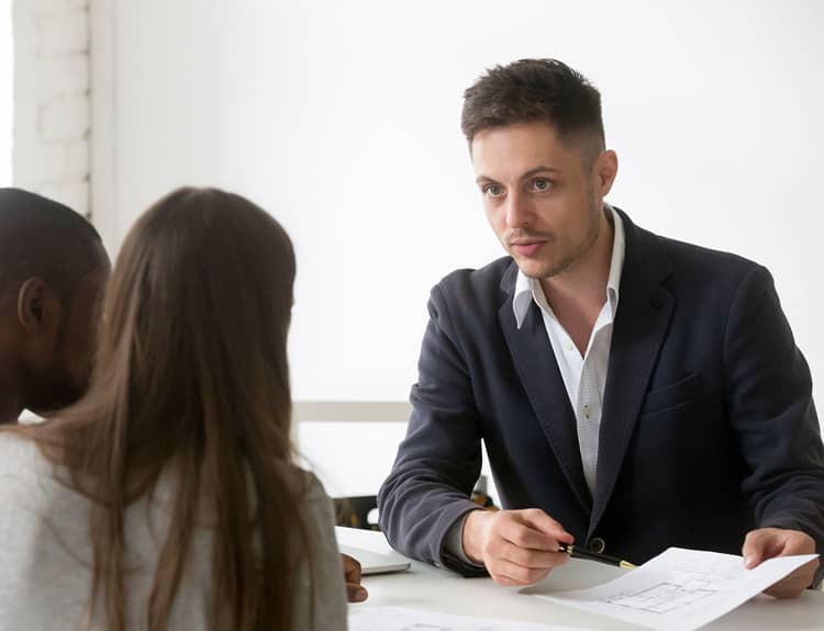 Un homme en costume parle à une femme assise à une table.