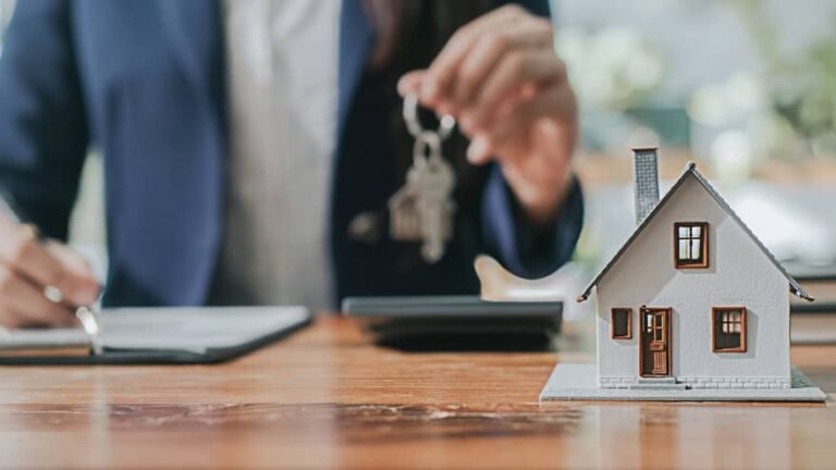 Une femme tenant la clé d’une maison modèle sur un bureau.