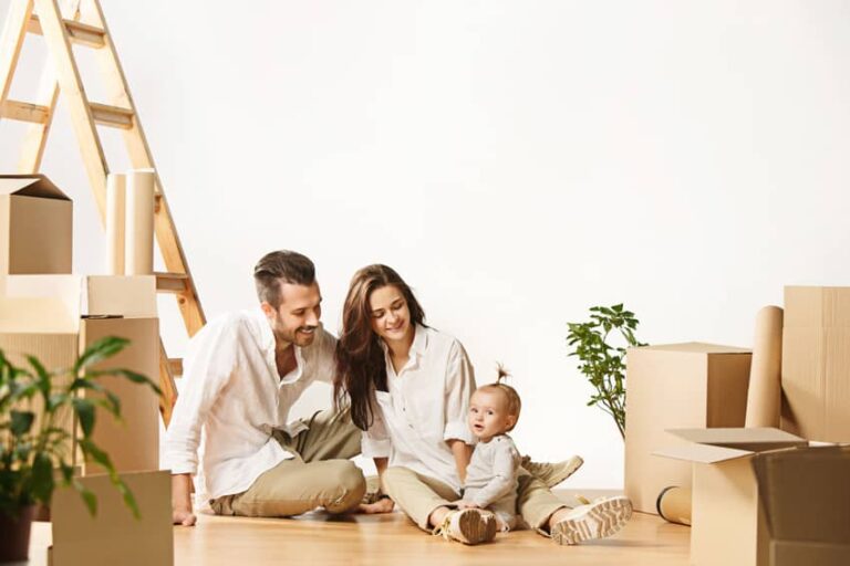 Une famille avec un bébé assis par terre devant des cartons de déménagement.